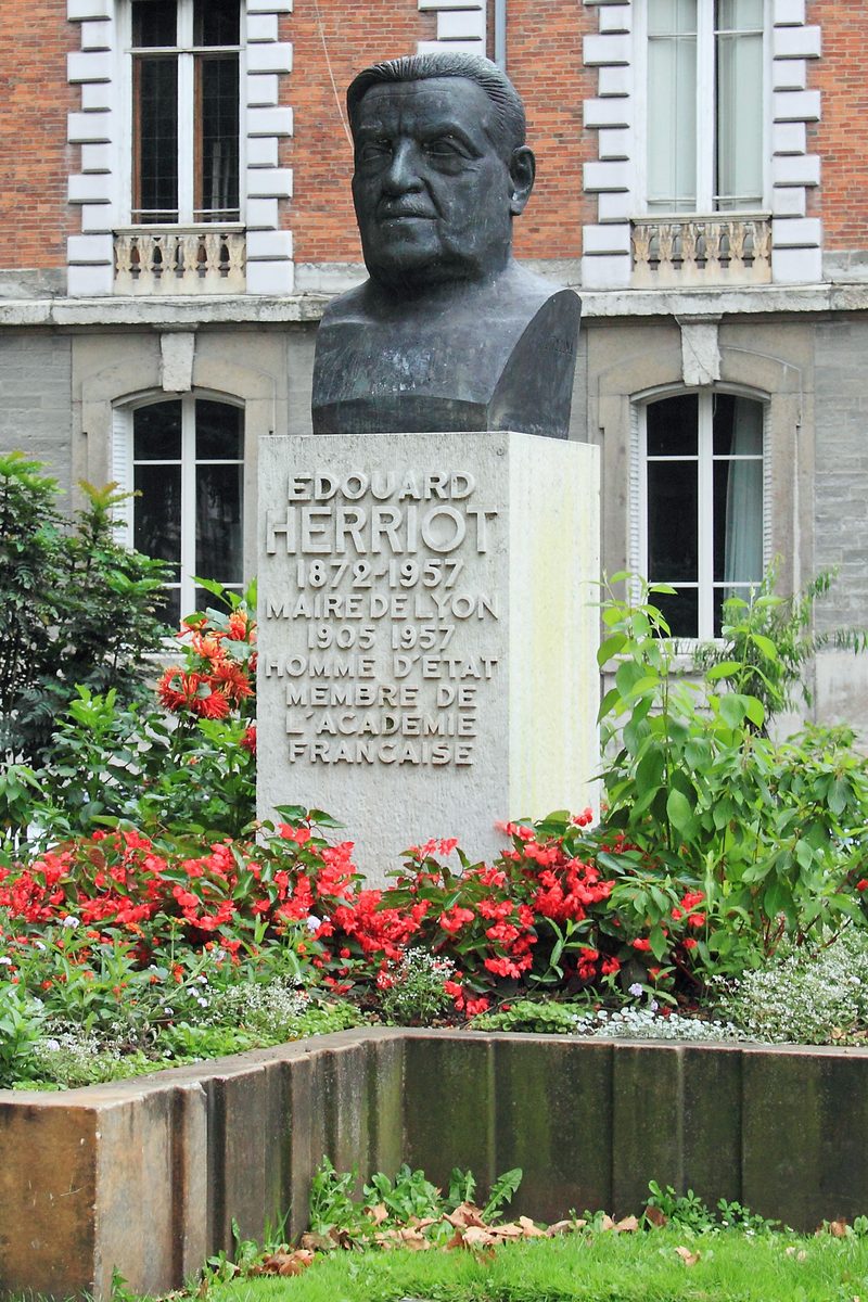 Buste d’Édouard Herriot sur un socle de pierre gravé, entouré de massifs fleuris